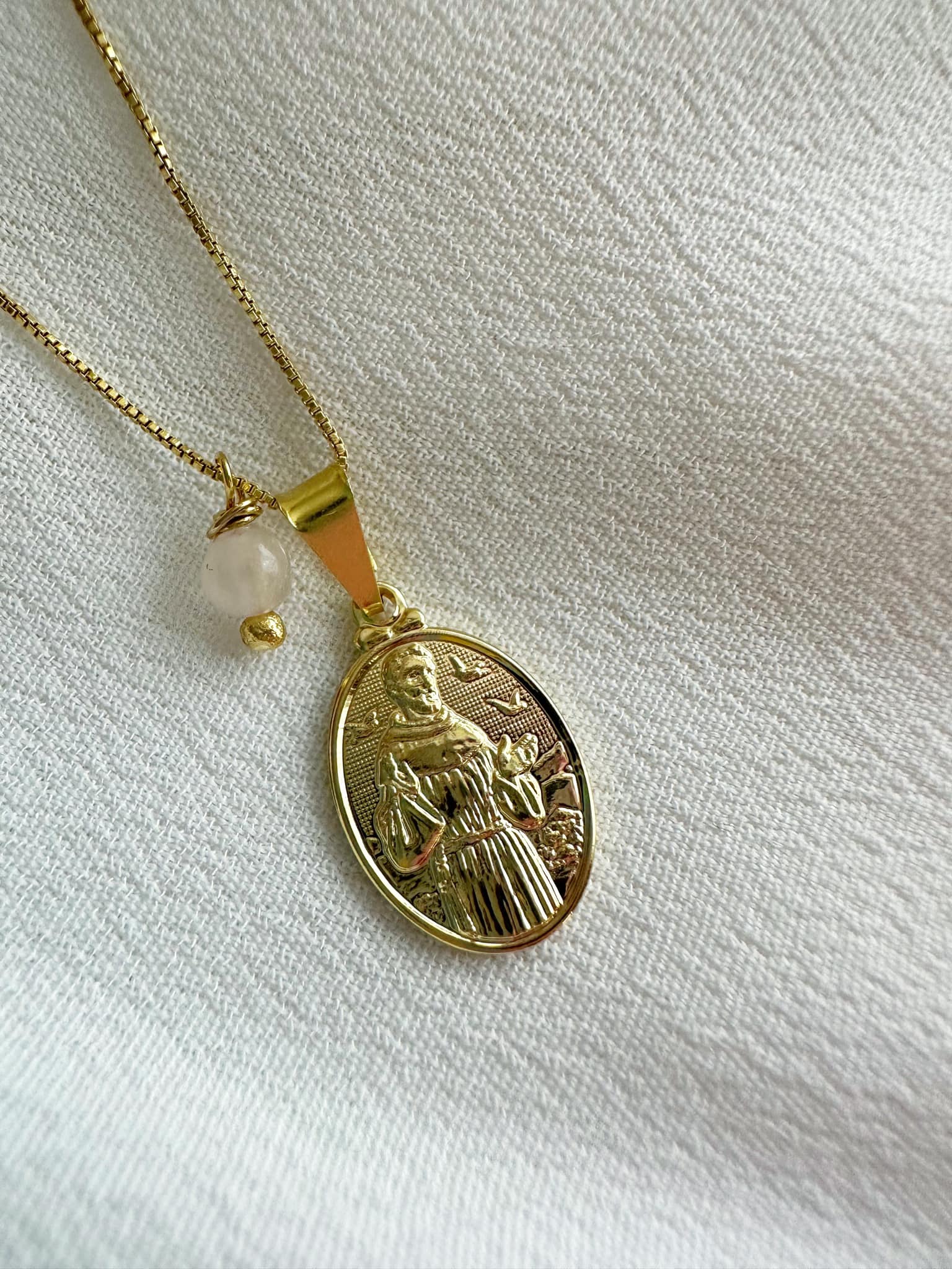 collar de mujer baño de oro 18k con medalla de san francisco de asis acompañado de una pequeña perlita de cuarzo rosa 